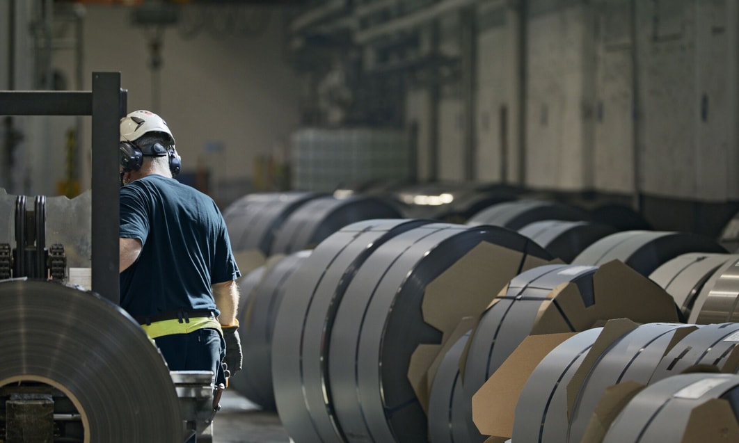 a person wearing a helmet and standing next to rolls of steel