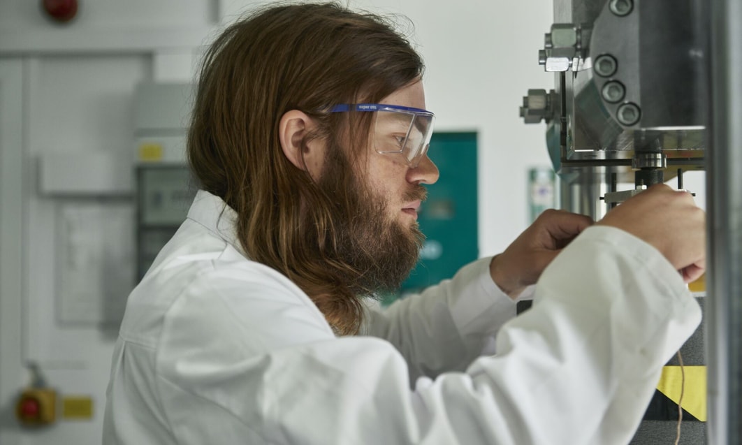 a person wearing goggles and white coat working on a machine