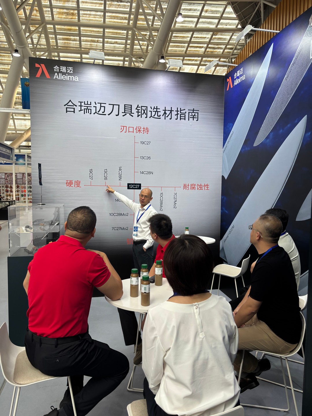 A man from Alleima displays Alleima's steel grades on large poster with people sitting around it